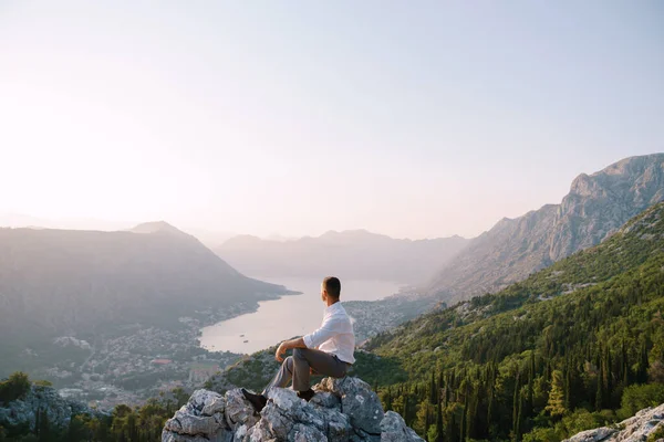 Bräutigam sitzt auf einem Felsen und blickt auf das Bergpanorama, das Meer und das Grün — Stockfoto