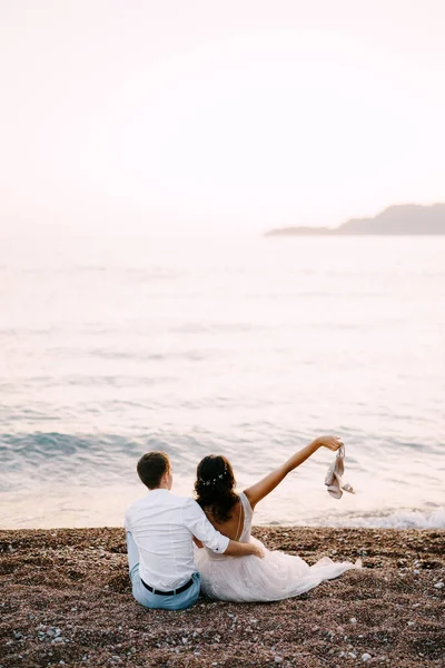 Groom étreint mariée tout en étant assis sur la plage de sable près de la mer. Vue arrière — Photo