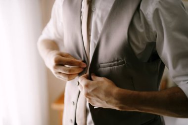 Gömlekli ve kravatlı bir adam yeleğinin düğmelerini ilikliyor. Yakın plan.