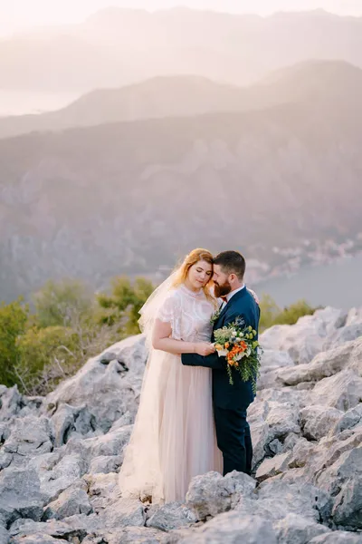 Mariée et marié étreignant sur une montagne rocheuse au-dessus de la mer — Photo