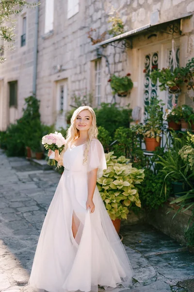A bride with a bouquet in her hands stands on a cozy street of the old city near a porch of a house — Stock Photo, Image