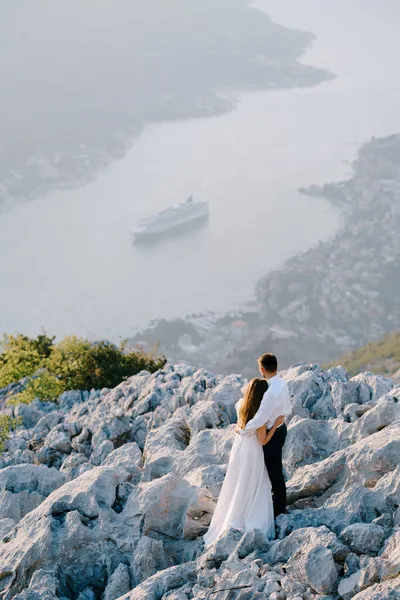 Époux étreint mariée sur une colline de pierre et regarde la baie de Kotor — Photo
