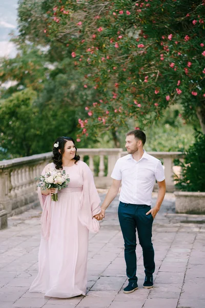 Невеста в розовом платье с букетом держит жениха за руку — стоковое фото
