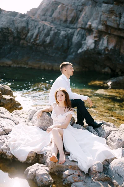 Novia y novio se sientan en las piedras contra el telón de fondo de un acantilado rocoso —  Fotos de Stock