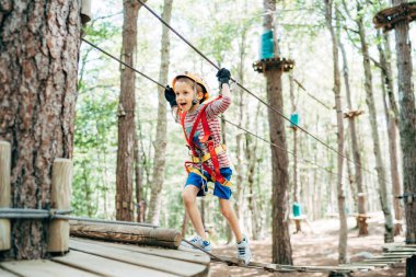 Çocuk çeviklik köprüsünden geçerek ağaçtaki platforma yürüyor.