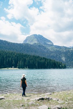 Kadın körfezin kıyısında duruyor ve dağlara bakıyor. Arka plan