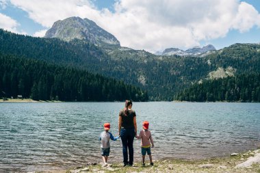 Kadın denizin kıyısında durur ve çocukları ellerinden tutar. Arka plan
