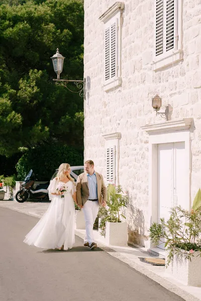Braut und Bräutigam gehen an einem Steinhaus mit grünen Pflanzen vorbei — Stockfoto