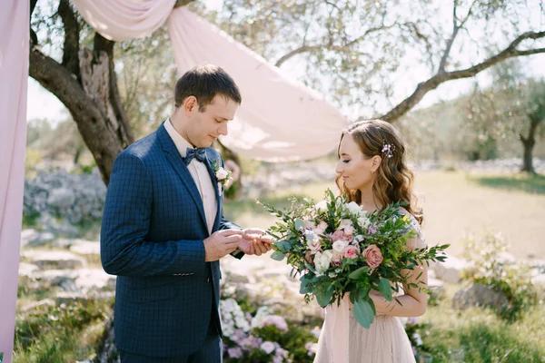 Groom met une bague sur le doigt de la mariée avec un bouquet dans le parc — Photo