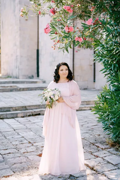 A noiva com um buquê de flores está abaixo de uma árvore florescente em um pavimento — Fotografia de Stock