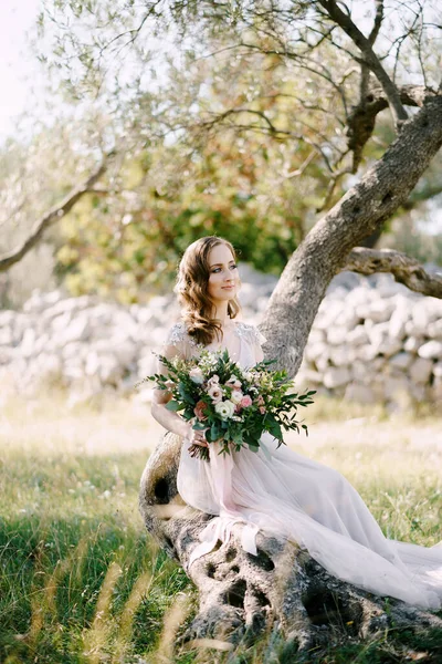 Nevěsta sedí na kmeni stromu s kyticí — Stock fotografie