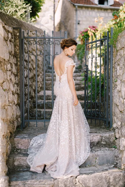 Menyasszony egy ruha áll a kő lépcsőn előtt a kovácsolt kapu a ház — Stock Fotó