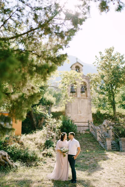 Жених обнимает невесту в парке на фоне маленькой колокольни — стоковое фото