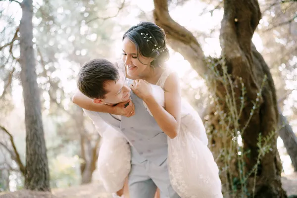 Невеста спрыгнула на жениха. Жених и невеста веселятся среди деревьев в оливковой роще — стоковое фото