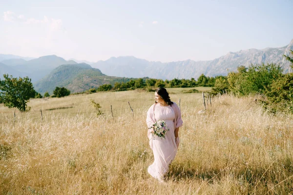 山を背景に花畑に花の花束を持つ花嫁 — ストック写真