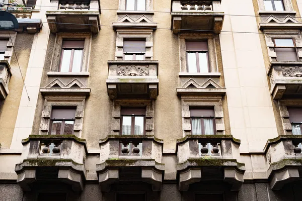 Fasada starego domu z rzeźbionymi kamiennymi balkonami i okiennicami na oknach. Mediolan, Włochy — Zdjęcie stockowe