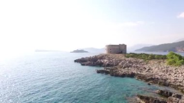 Kayalık bir sahildeki Arza kalesindeki hava manzarası yeşil dağların arka planına karşı.