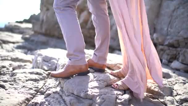 ズボンと花嫁の新郎は、風になびくドレスで岩の海岸に立っている。閉鎖 — ストック動画