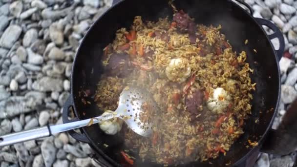 Котел с узбекским пловом и ложкой на плите — стоковое видео