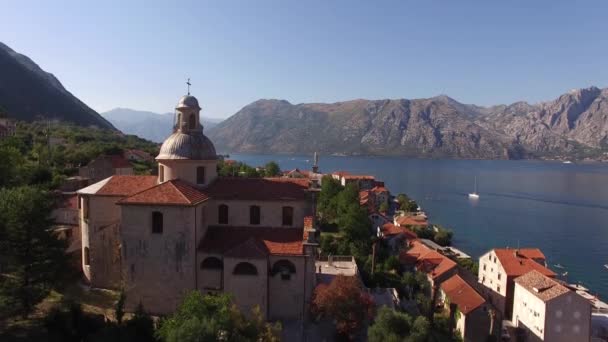 Kerk van Onze Lieve Vrouw Geboorte tegen de achtergrond van gebouwen van Prcanj en de baai van Kotor — Stockvideo