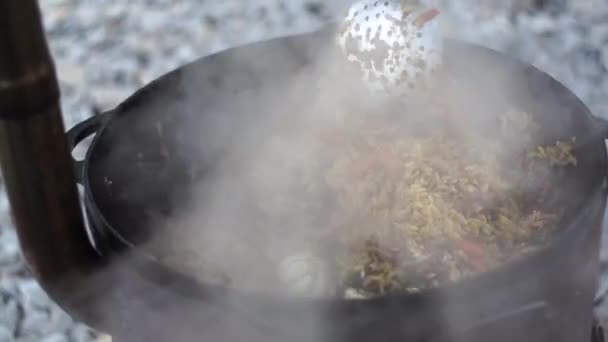 Agitar pilaf uzbeko con cabezas de ajo en un caldero — Vídeo de stock