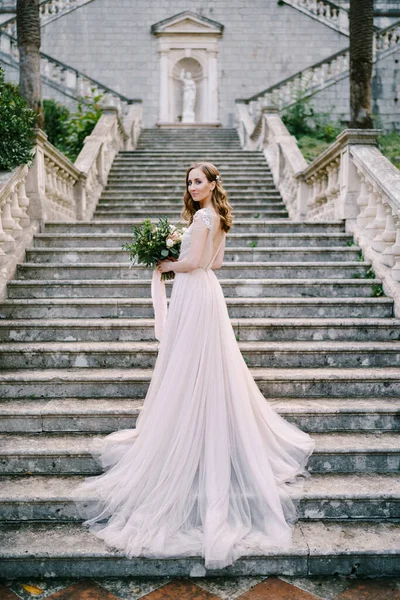 Nevěsta v dlouhých šatech stojí zpola zabalená na kamenných schodech — Stock fotografie