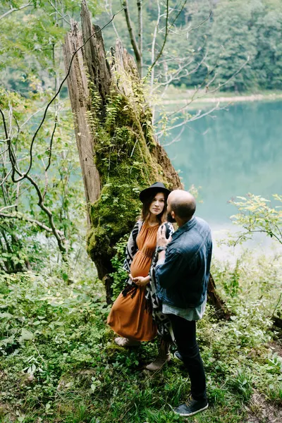 Hombre y una mujer embarazada de pie cerca de un árbol cubierto de musgo junto al lago —  Fotos de Stock