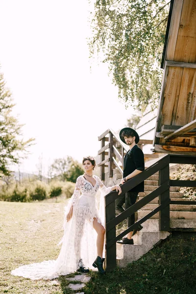 Noivo e noiva ficar nos degraus de pedra perto da cabana de madeira — Fotografia de Stock
