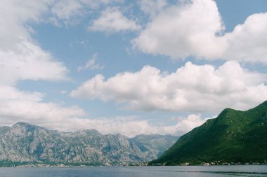 Mavi gökyüzünde beyaz bulutlar yeşil dağların arka planına karşı. Perast 'tan Görünüm