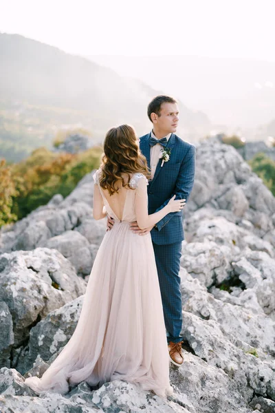 Sposo abbraccia sposa dalla vita su una montagna rocciosa — Foto Stock