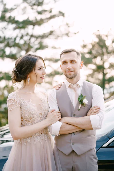 Η νύφη αγκαλιάζει τον γαμπρό δίπλα στο αυτοκίνητο. — Φωτογραφία Αρχείου