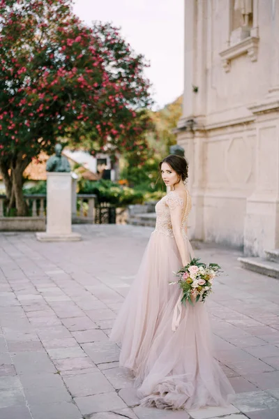 Bruid met een boeket bloemen staat vlakbij een oud gebouw in de tuin — Stockfoto