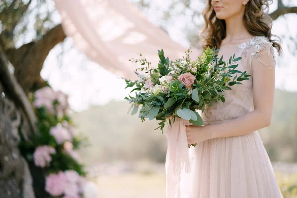 Η νύφη με ένα μπουκέτο λουλούδια στα χέρια της στέκεται κάτω από ένα δέντρο. Κοντινό πλάνο — Φωτογραφία Αρχείου