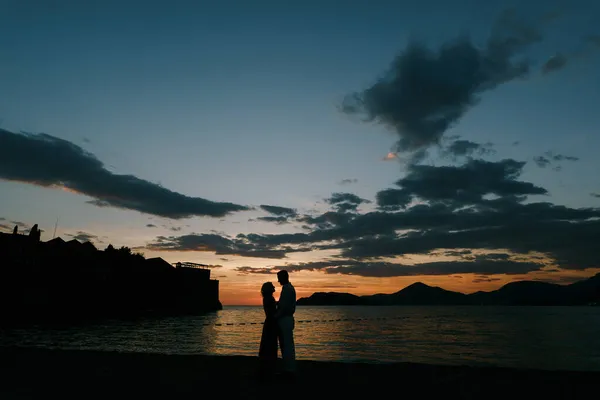 Чоловік обіймає жінку на березі затоки на заході сонця — стокове фото