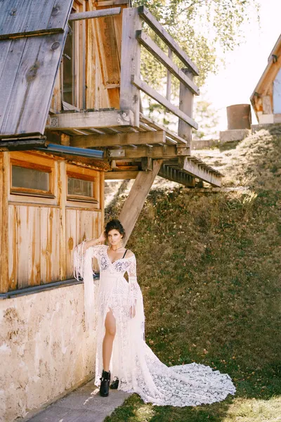 身穿白色花边裙的年轻女子站在一座古老的木头房子旁边 — 图库照片