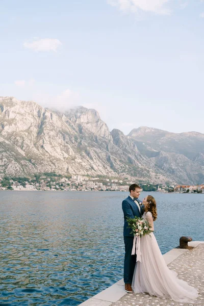 Pengantin pria memeluk pengantin wanita di dermaga dengan latar belakang pegunungan — Stok Foto