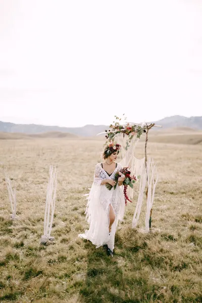 Noiva em uma grinalda com um buquê de flores está andando perto do arco de casamento — Fotografia de Stock