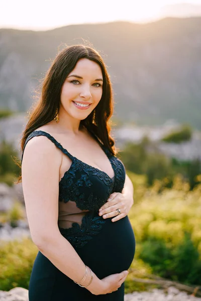 Έγκυος γυναίκα αγκαλιάζει την κοιλιά της στέκεται στην κορυφή ενός βραχώδους βουνού — Φωτογραφία Αρχείου