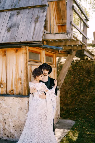 Noivo abraços noiva em um vestido de renda branca perto da velha casa de madeira — Fotografia de Stock