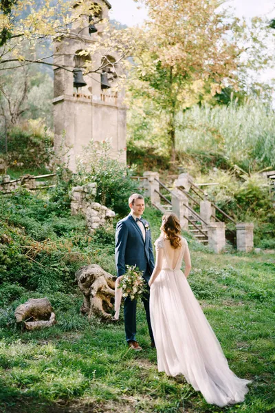 Pengantin wanita pergi ke pengantin pria dengan karangan bunga dekat kapel tua di taman — Stok Foto