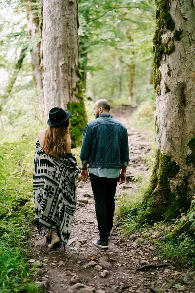 Mujer en una capa y sombrero camina con un hombre entre los árboles en un parque verde. Vista trasera —  Fotos de Stock