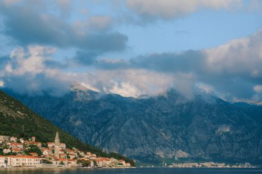 Bulutlu bir gökyüzüne karşı eski evlerle dolu kıyı şeridi. Karadağ