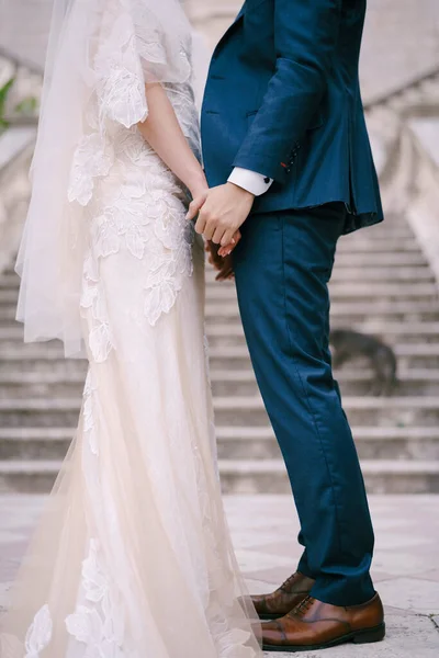 Наречений і наречений стоять, тримаючись за руки на кам'яних сходах. Крупним планом — стокове фото