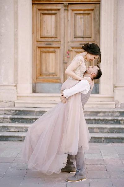 Pengantin pria memegang pengantin wanita di tangannya di depan pintu masuk ke bangunan kuno — Stok Foto