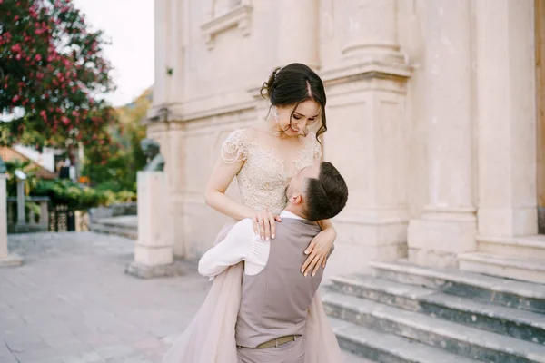 A vőlegény a karjaiban tartja a menyasszonyt a régi épület márvány homlokzata előtt. — Stock Fotó
