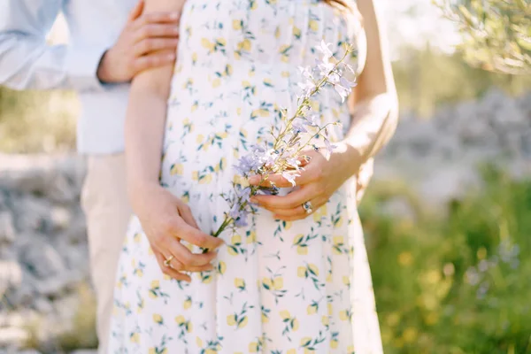 Un homme serre une femme enceinte tenant des fleurs sauvages. Gros plan — Photo