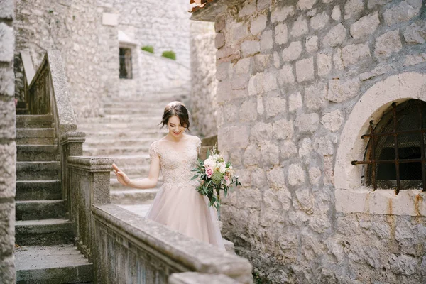 A menyasszony egy csokorral leereszkedik egy kőépület lépcsőjén. — Stock Fotó
