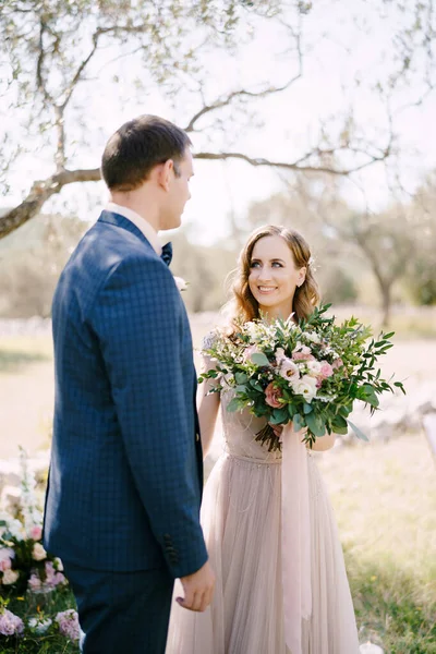 Pengantin pria berdiri dengan pengantin wanita tersenyum dengan karangan bunga di kebun hijau — Stok Foto
