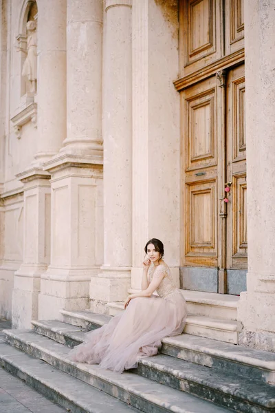 Noiva senta-se nos degraus de um edifício velho em frente à entrada — Fotografia de Stock