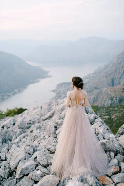 Noiva fica em uma montanha rochosa contra o pano de fundo da Baía Kotor. Visão traseira — Fotografia de Stock